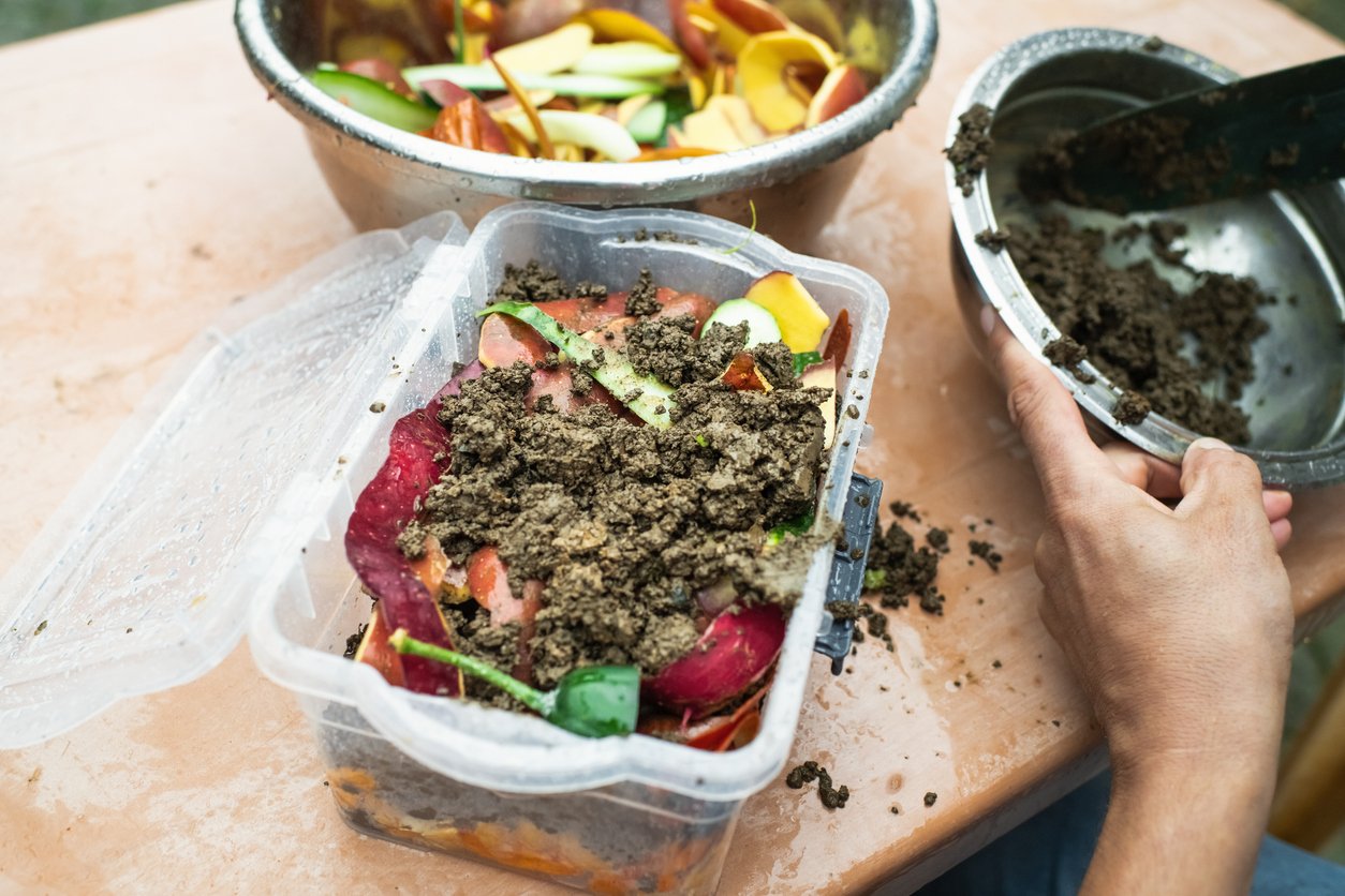 Man making compost from leftovers at an open kitchen outdoors at back yard. Sustainable lifestyle and zero waste cooking concept.