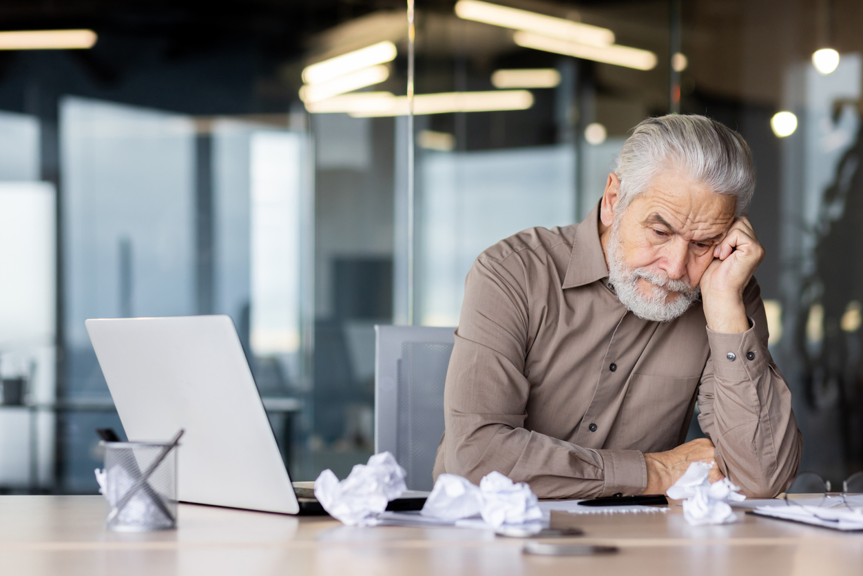 Upset frustrated gray haired boss sitting inside office at workplace, mature man old businessman in shirt working with laptop, unhappy with company achievement results and negative reports.