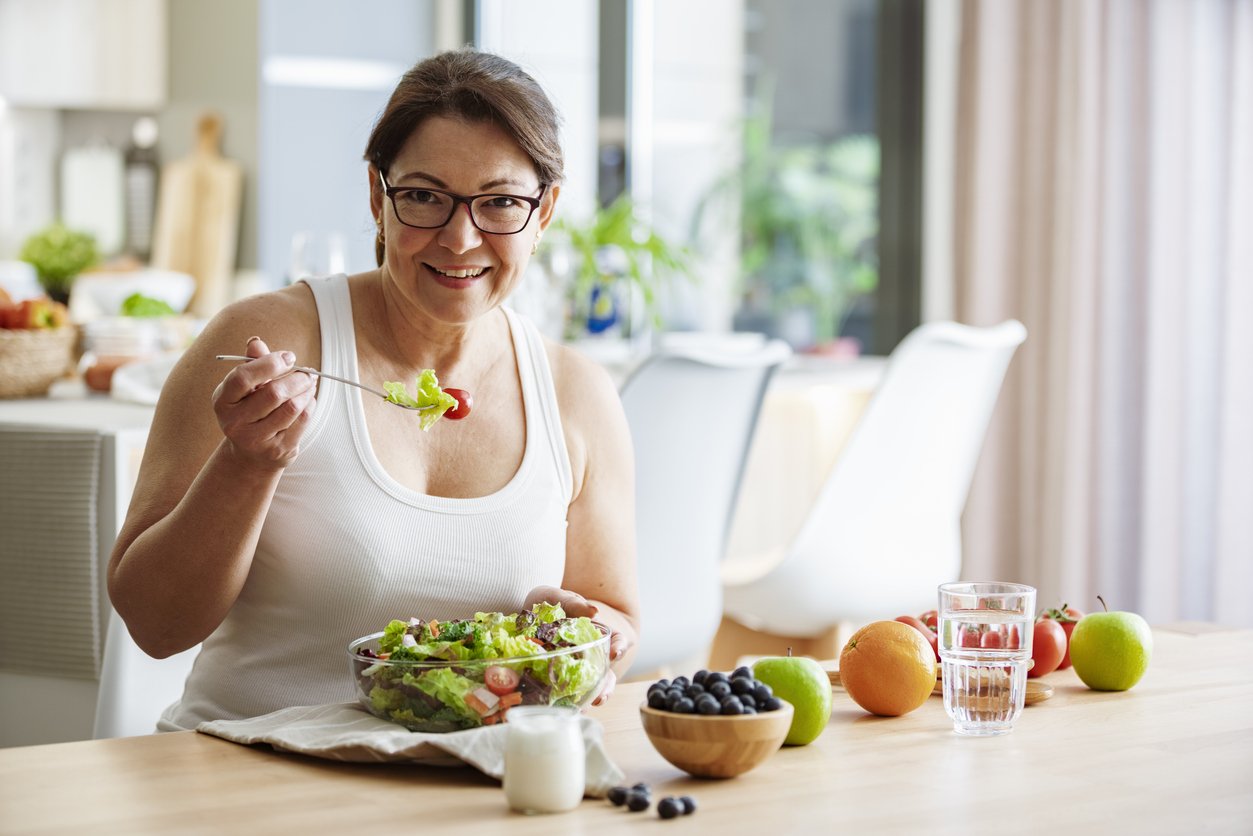 Confident woman looking at camera eating a healthy salad and fruits. High resolution 42Mp indoors digital capture taken with Sony A7rII and Canon EF 70-200mm f/2.8L IS II USM Telephoto Zoom Lens