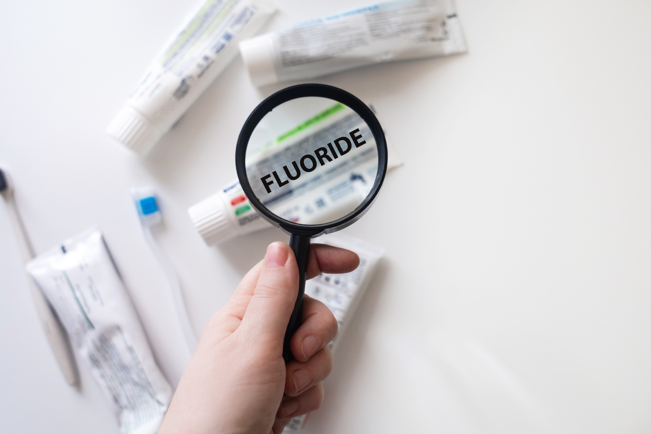 Checking the composition of toothpaste with a magnifying glass against the background of many tubes. Dangerous toothpaste ingredient fluoride.