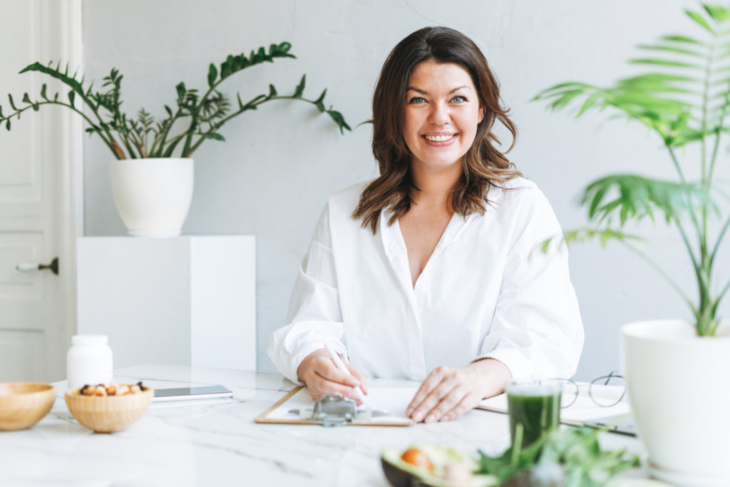 Female plant-based coach in all white sitting at a white table