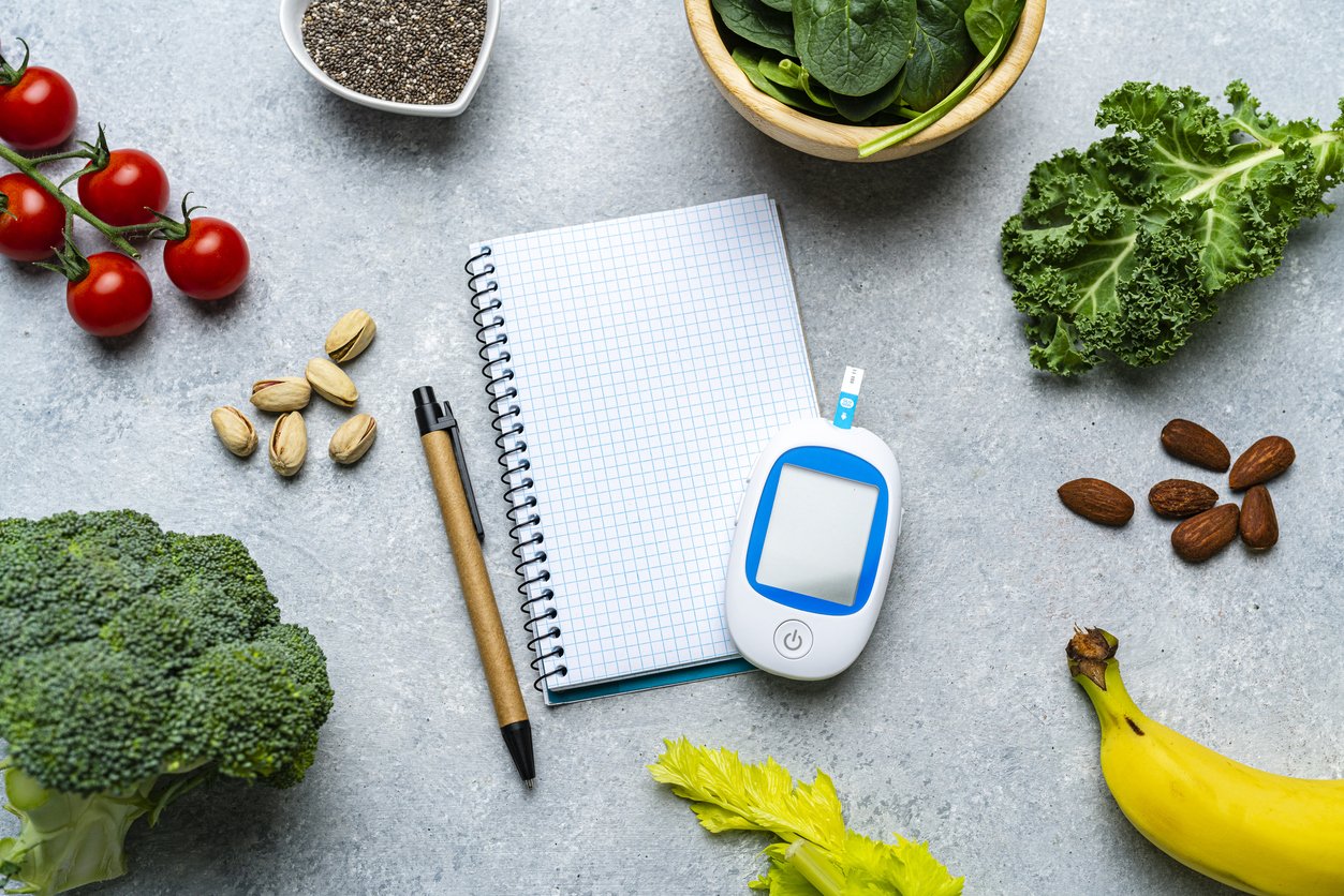 Glucometer, notepad and healthy vegetables for blood glucose control