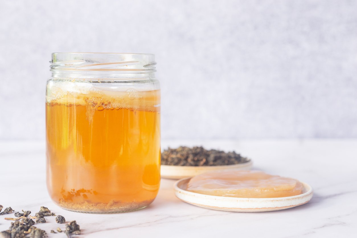 kombucha starter in a glass jar bottle with healthy Kombucha SCOBY symbiotic culture of bacteria and yeast in white ceramic plate and oolong loose leave tea on white  marble background, how to brew kombucha at home.