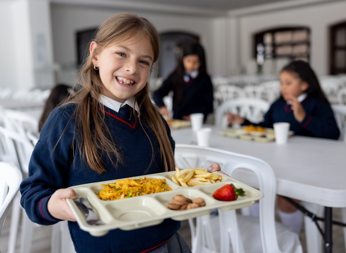 Happy Latin American schoolgirl carrying her school lunch at the cafeteria and looking at the camera smiling