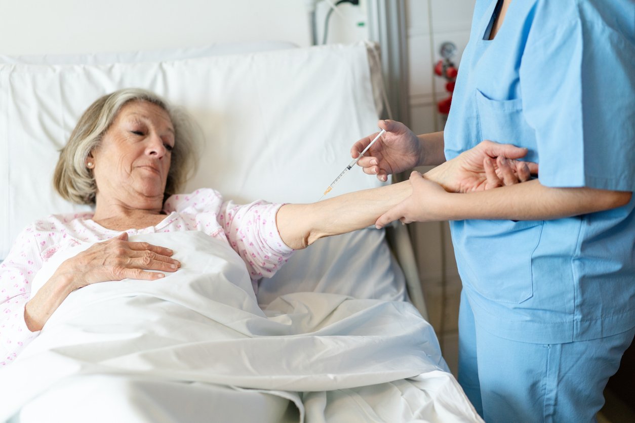 Nurse giving an injection to a senior woman patient in hospital, offering treatment and medical support during her recovery.