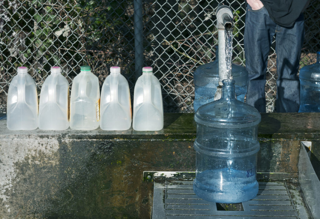 Person filling large water jugs with water out of a metal spigot