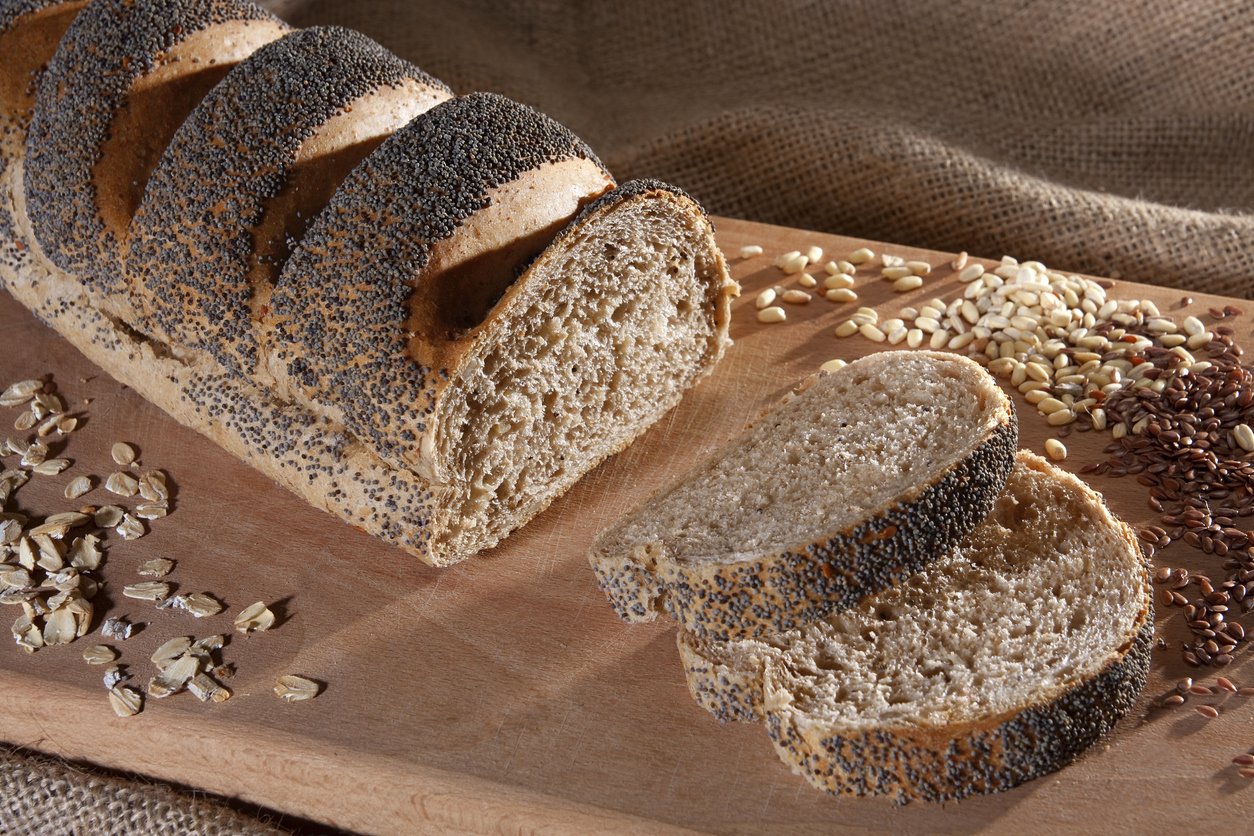 Slices of poppy seed bread with cereals and cutting board on sack background