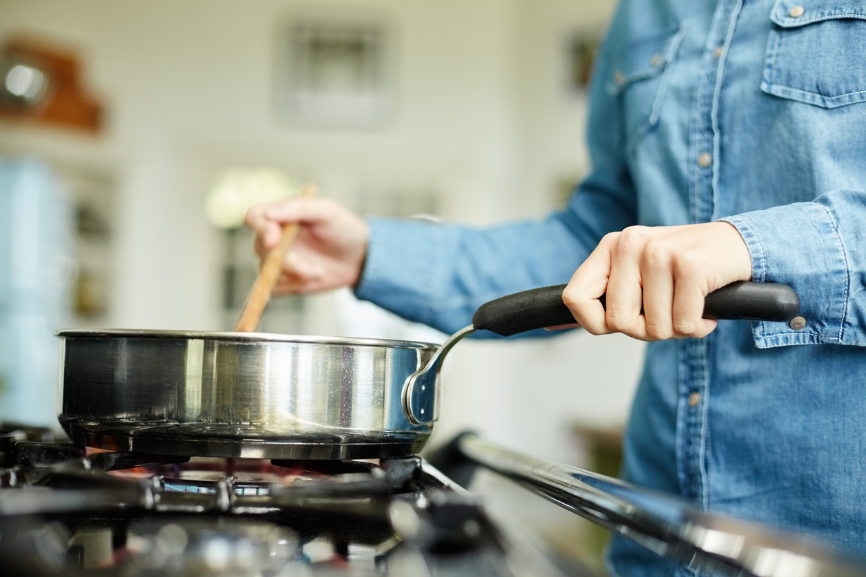 Woman cooking food with the kitchen tools, frying pan and wooden spoon.