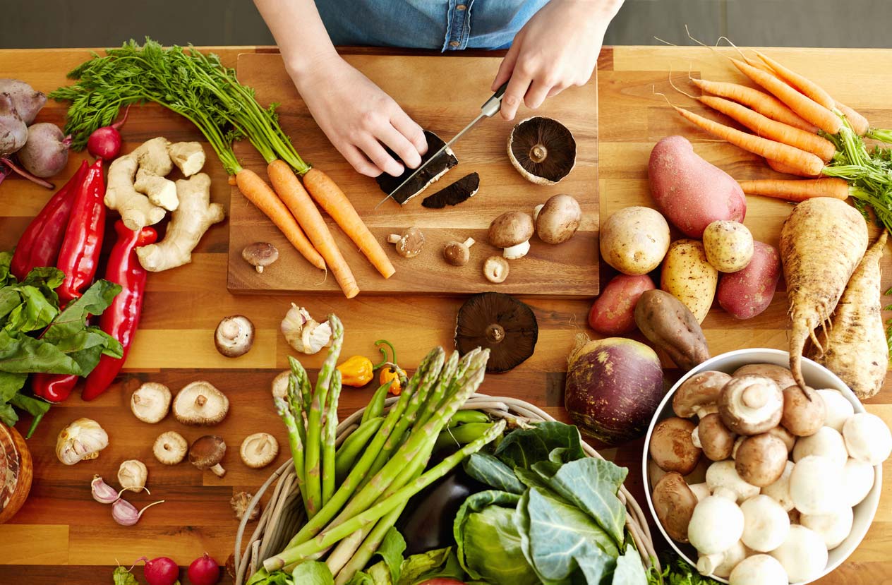 Hands cutting raw mushrooms on table of other veggies