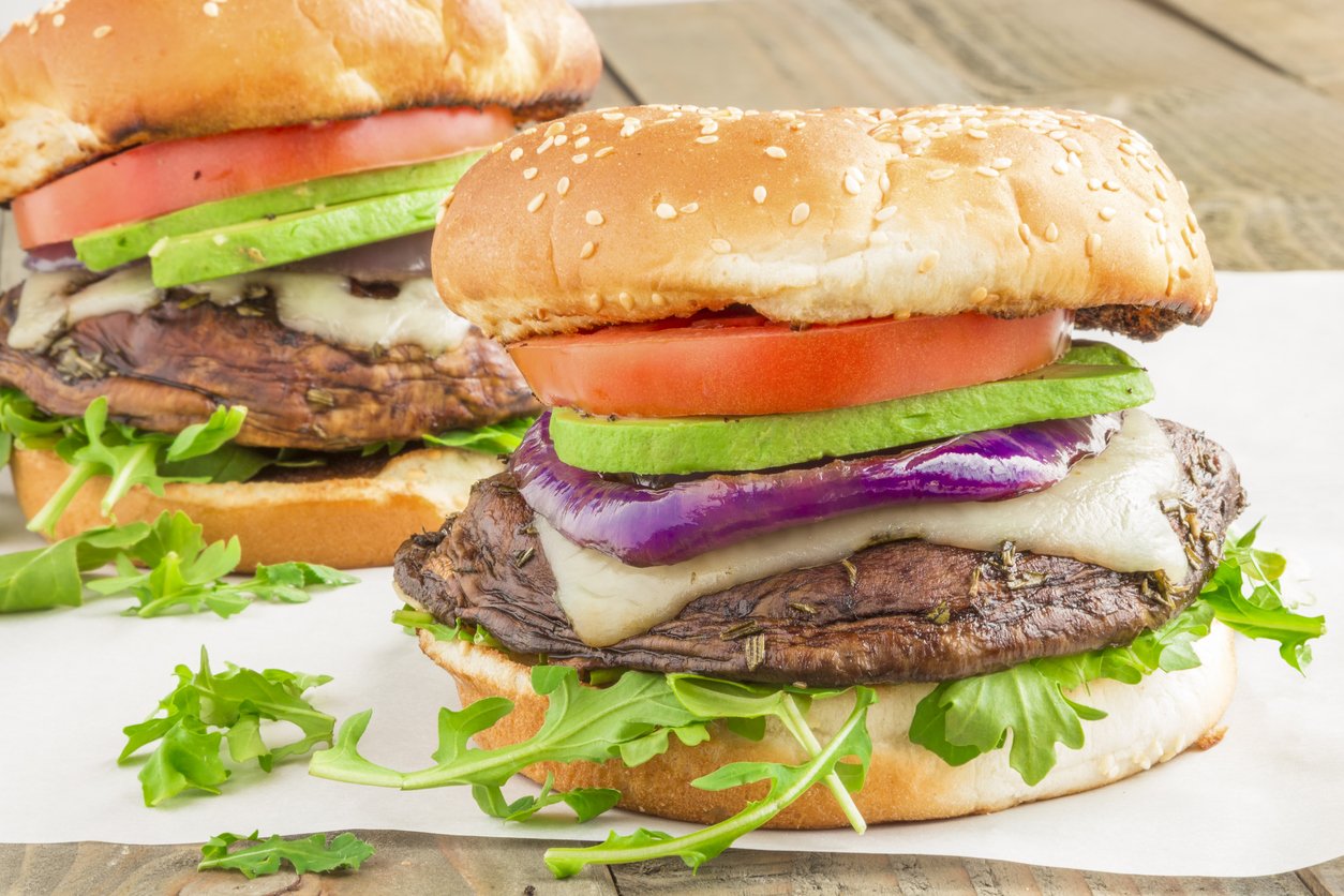 Portobello burgers on a bed of arugula, topped with melted swiss cheese, grilled purple onion, avocado and tomato