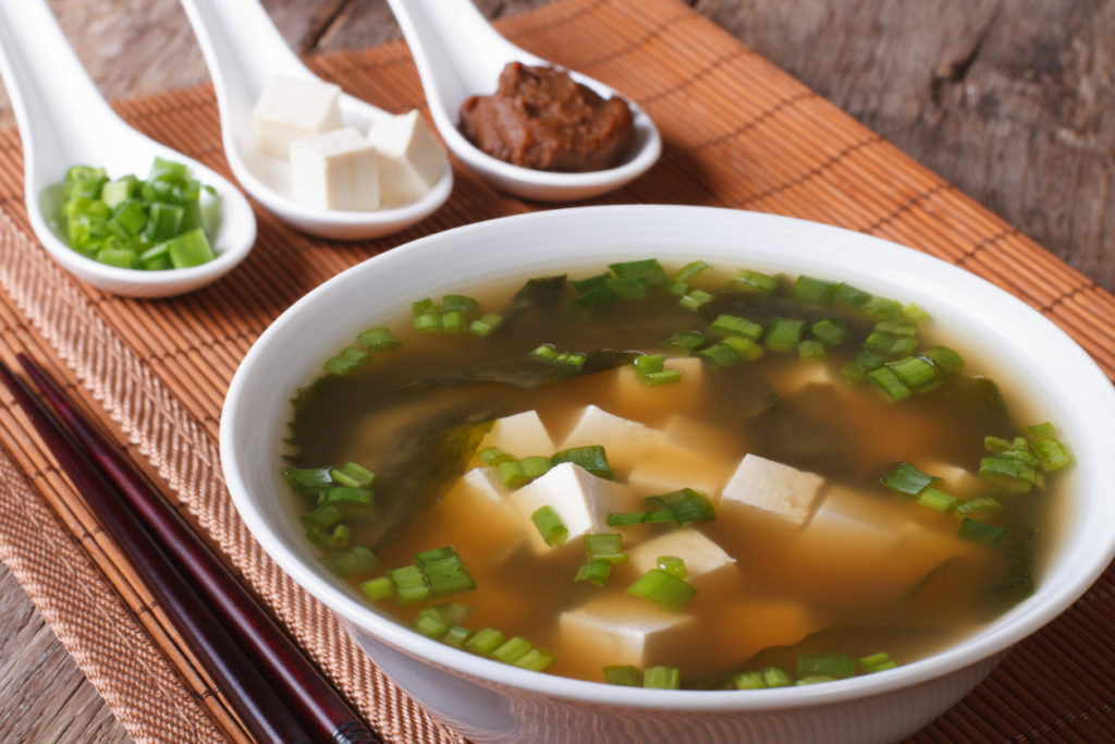 Japanese miso soup in a white bowl and ingredients in spoons