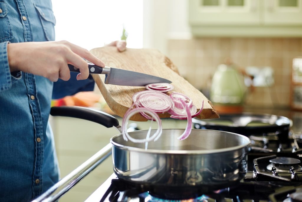 Cut onions going into a stainless steel skillet on the stove