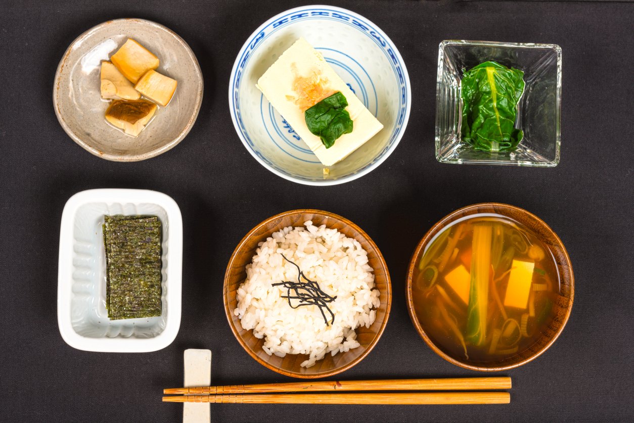 Japanese breakfast with a variety of foods, miso soup, rice, pickel, nori, various vegetables and tofu on black background.