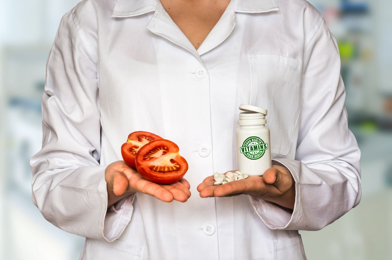 Young doctor holding tomato and bottle of pills with vitamins