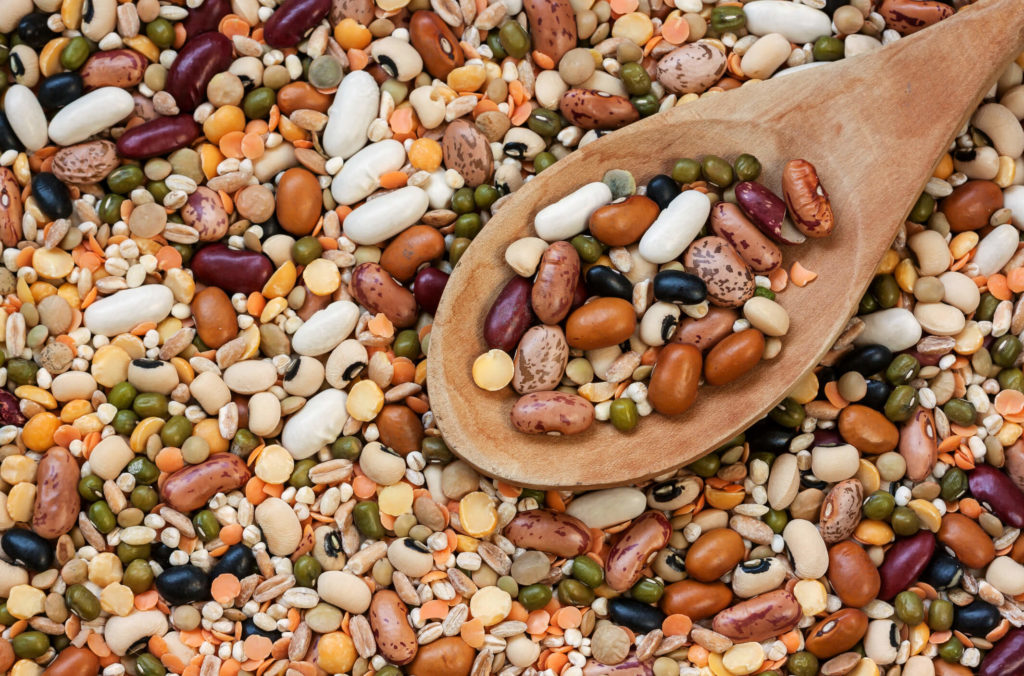 A variety of beans and legumes, with some on a wooden spoon