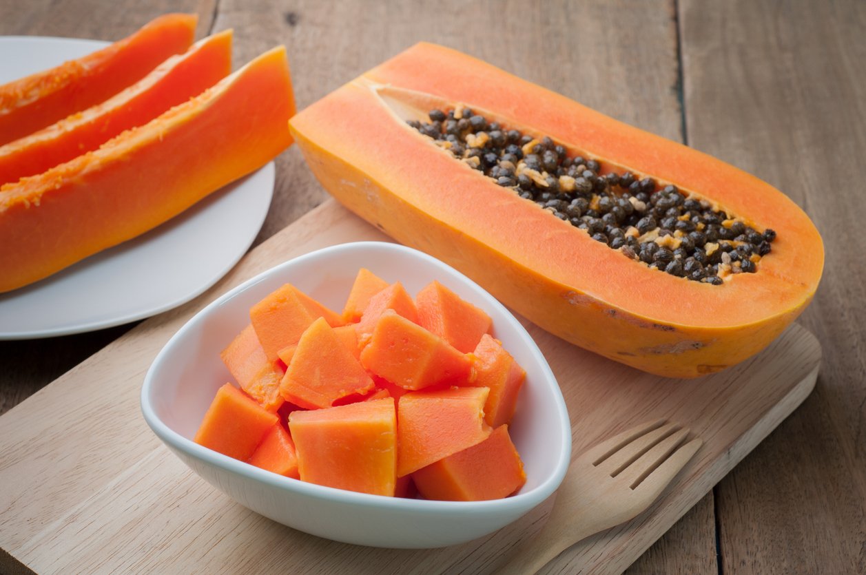 Sliced papaya fruit on white plates and wooden background.