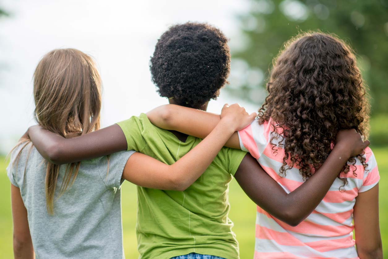 three young multi-racial friends standing together with arms on shoulders