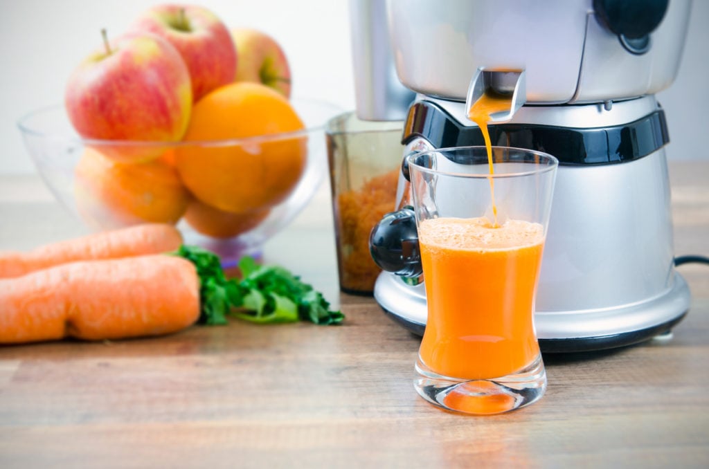 Fruits and vegetables next to a juicer showing juice and pulp