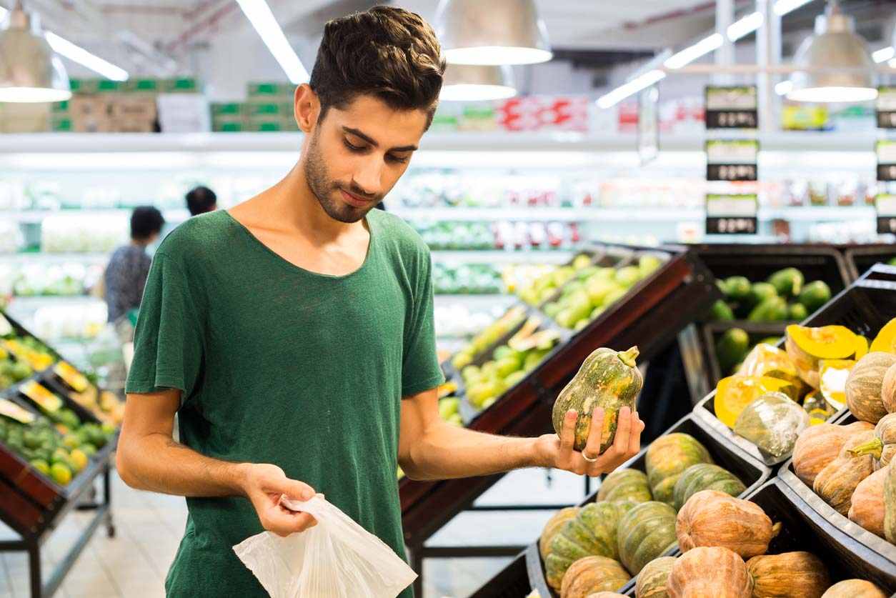 Guy picking out a winter squash in grocery store