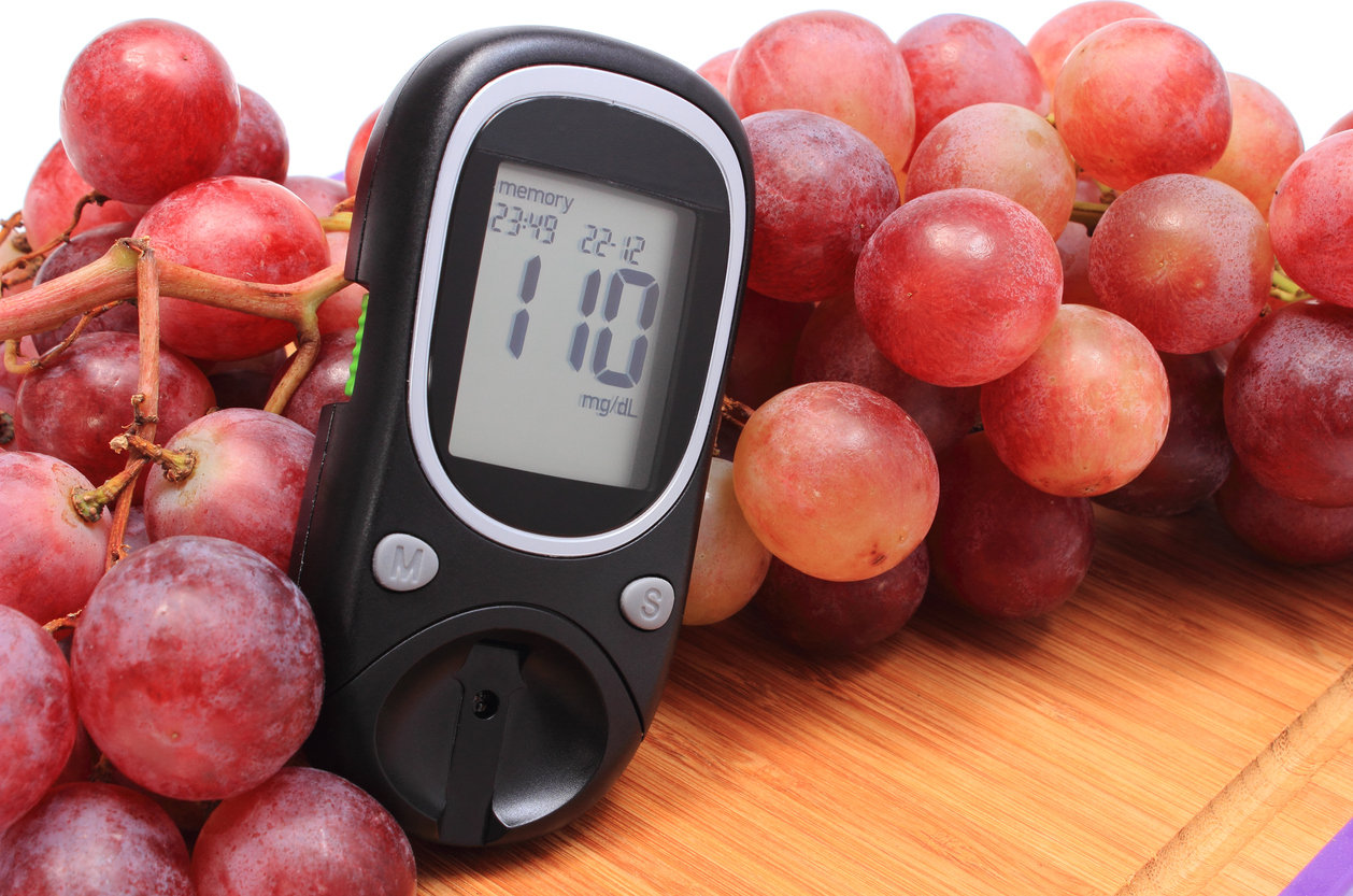Glucometer and fresh natural bunch of grapes on wooden cutting board, concept for healthy eating and diabetes