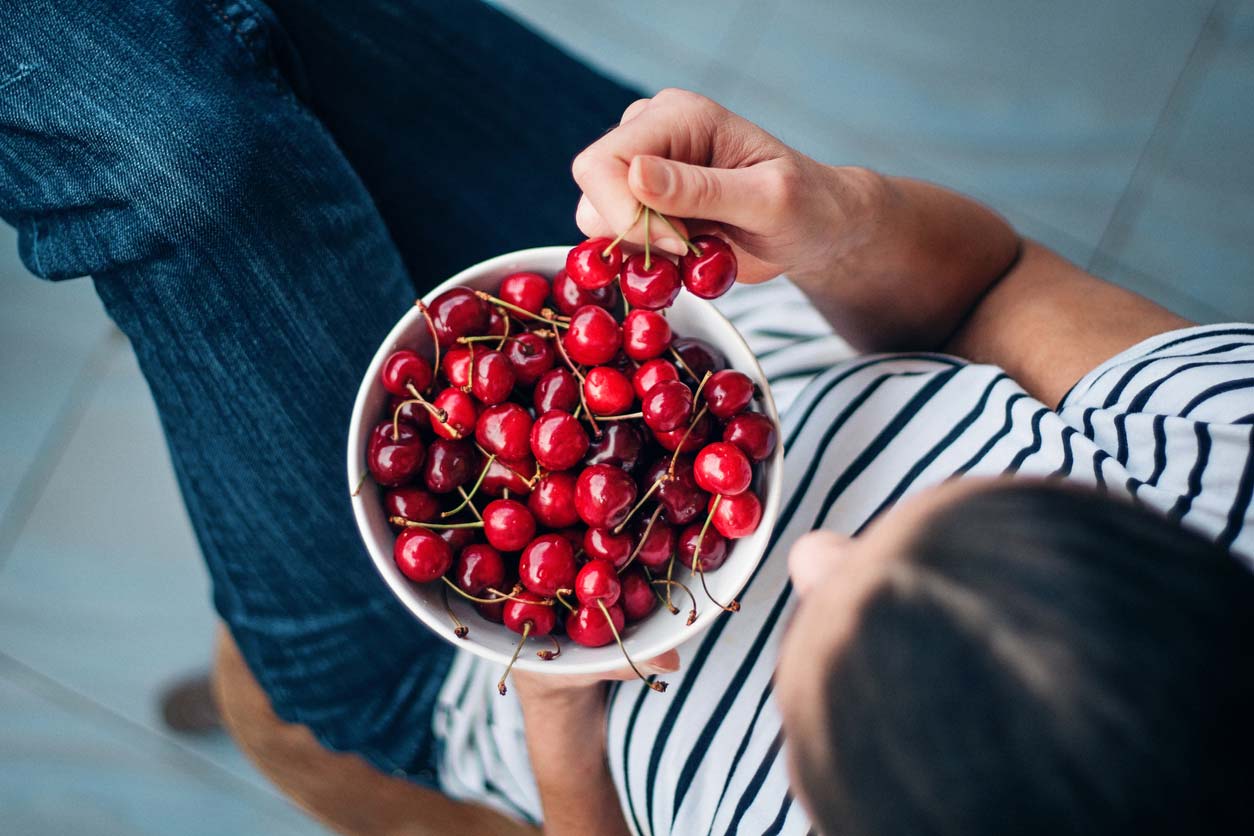 cherries in a bowl - woman enjoying benefits of cherries