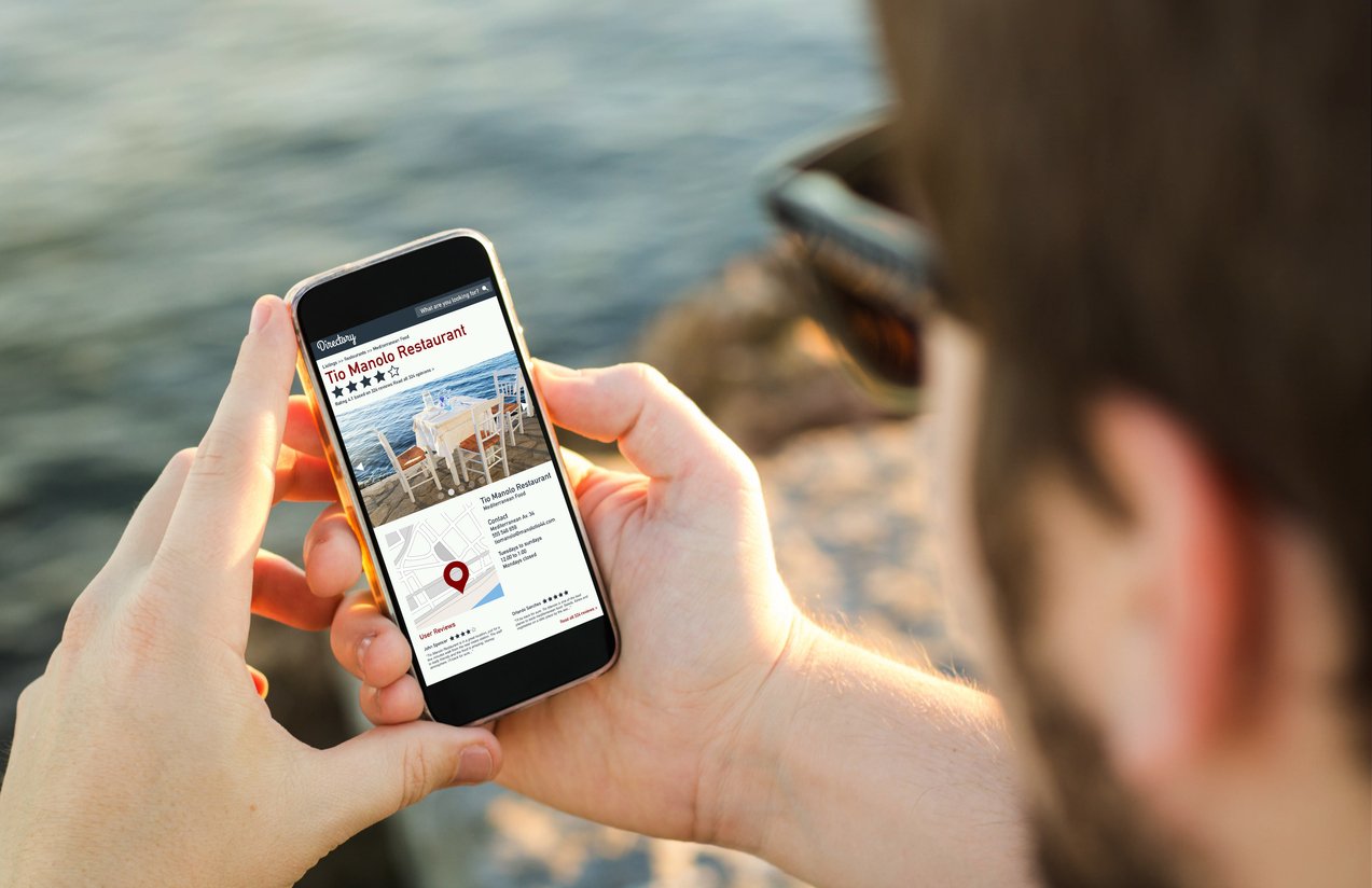 man on the coast using his smartphone browsing online directory. All screen graphics are made up.