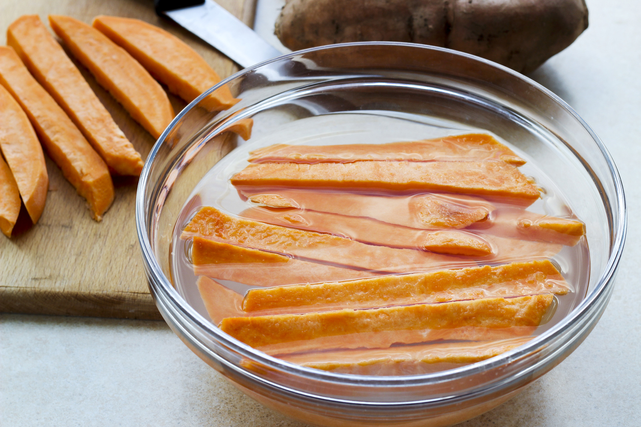 Fresh cut slices of sweet potatoes, made into fries, ready for cooking, bowl of water