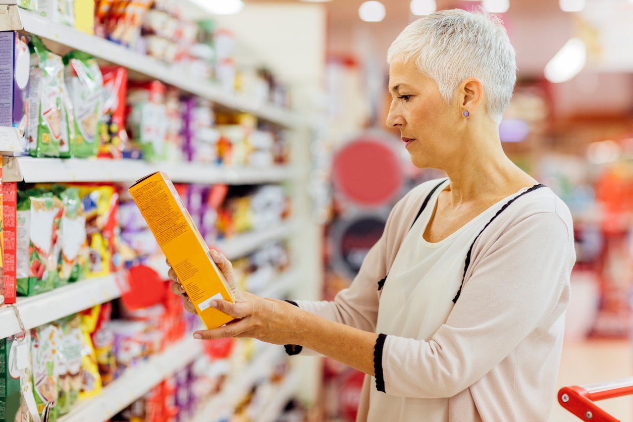 A woman looks at the ingredients on a box possibly looking for natural flavors