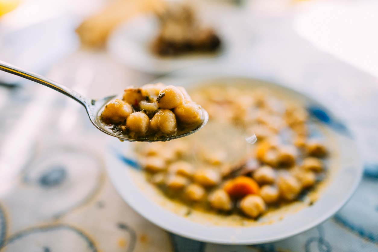 spoon holding chickpea soup above bowl