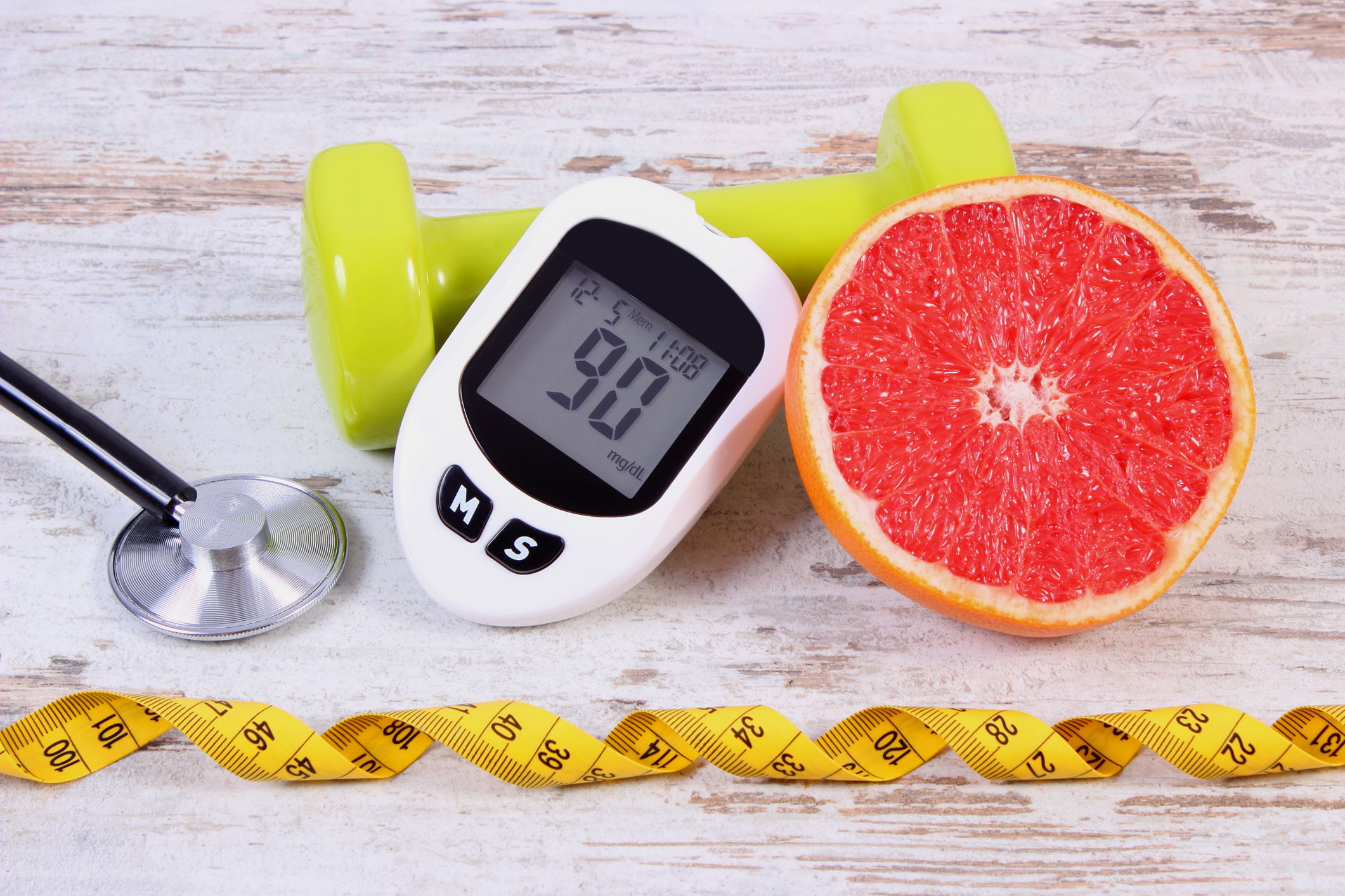 Glucose meter with result measurement sugar level, medical stethoscope, fresh grapefruit and green dumbbells for fitness, concept of diabetes, slimming, healthy lifestyles and nutrition