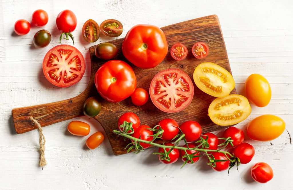 A variety of whole and sliced tomatoes on a cutting board