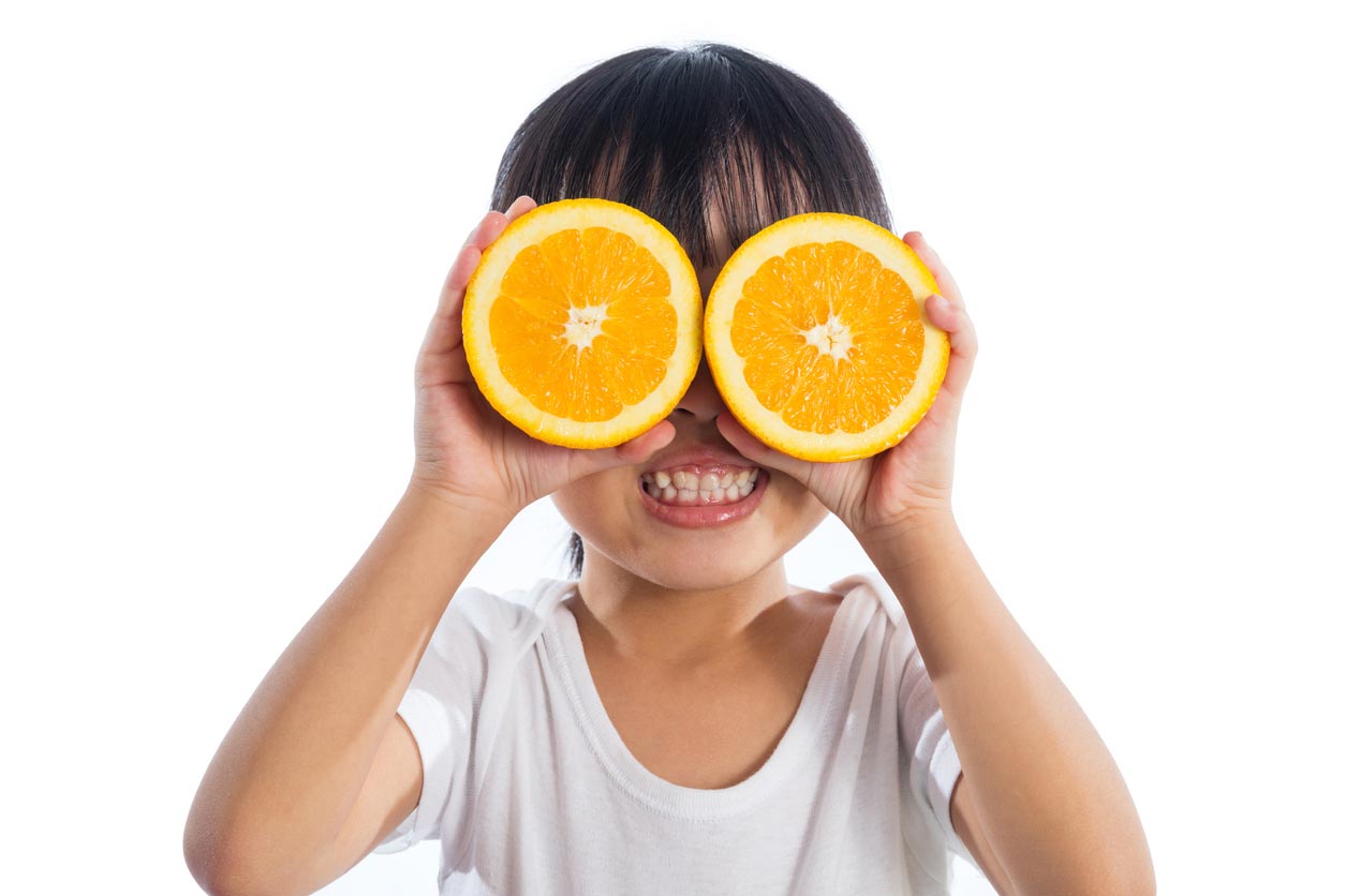 little girl using oranges as glasses