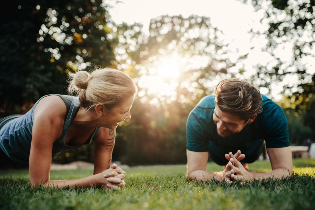 A man and woman doing planks in the grass outdoors