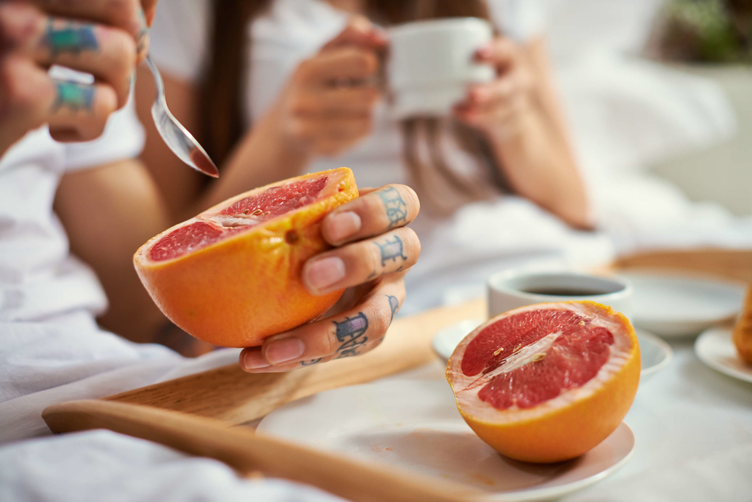Couple having healthy breakfast in bed, man eating grapefruit