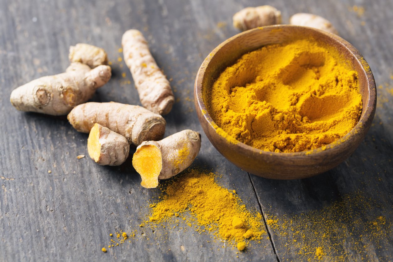 Freh turmeric roots and turmeric powder in a wooden bowl on rustic wood