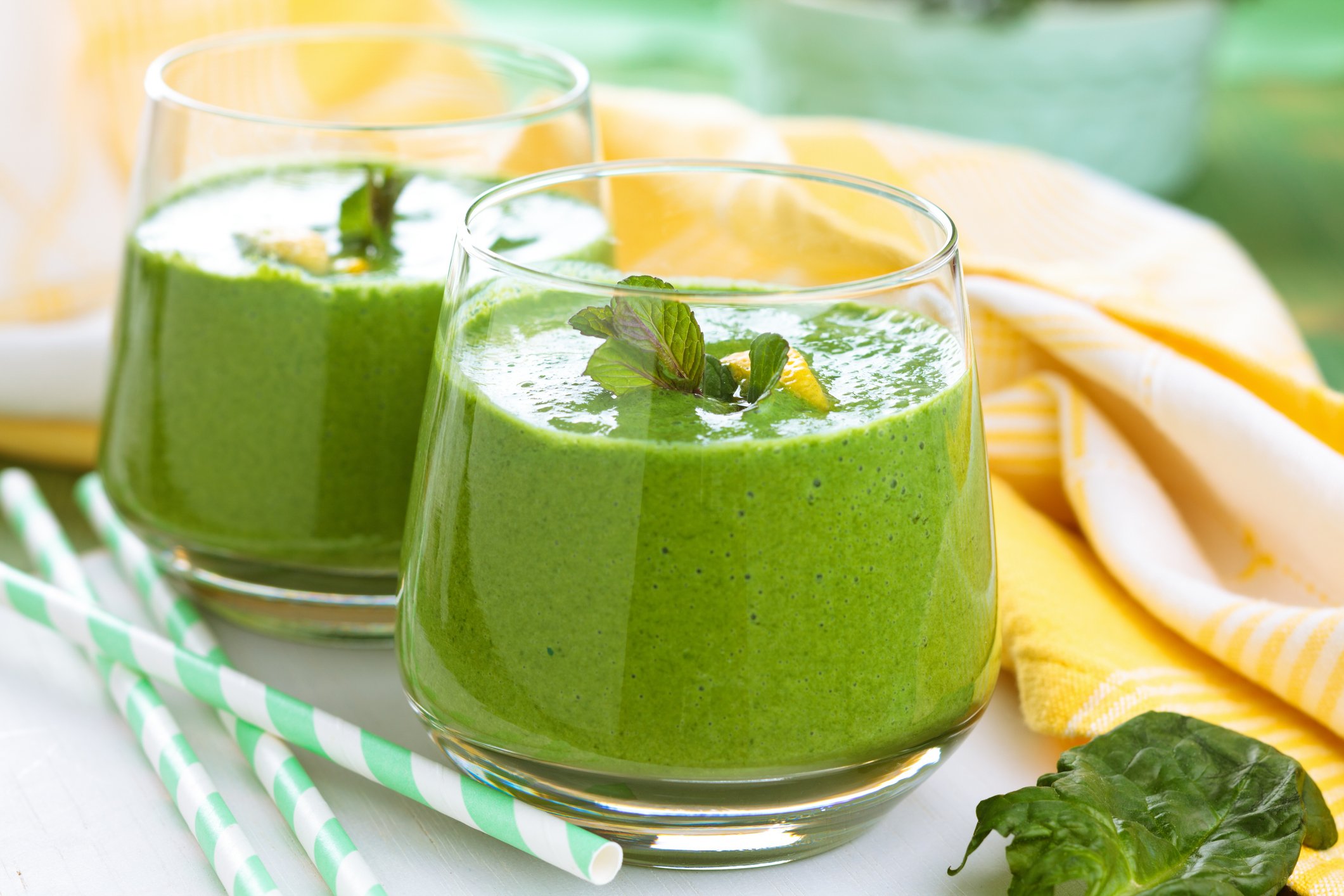 A pair of green smoothies with straws next to the glasses