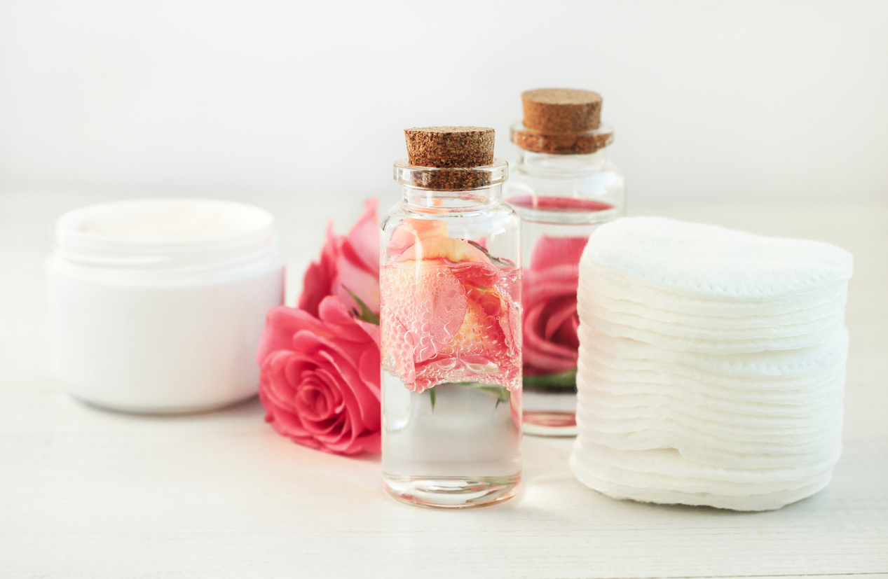 Glass bottle with attar bubbles and rose petals, cotton pads. Healing homemade skincare moisture toni