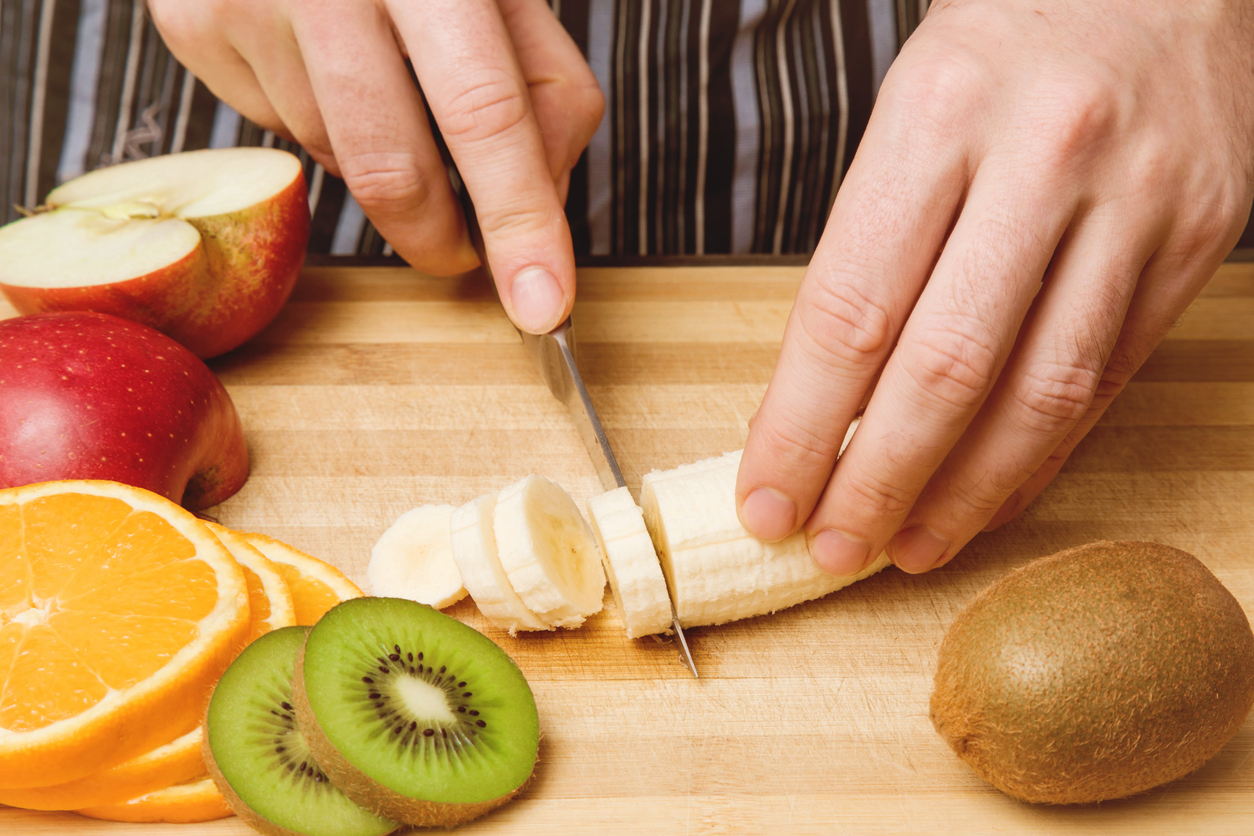 Man's hand with a knife cuts the banana. Healthy eating.