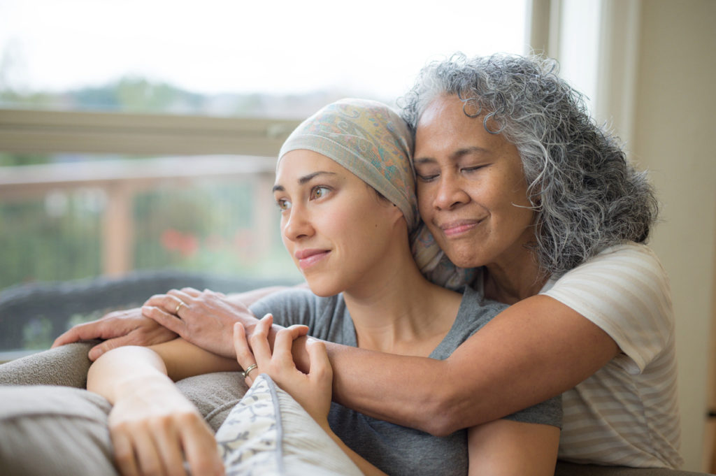 Mother embracing daughter with cancer who is looking out a window