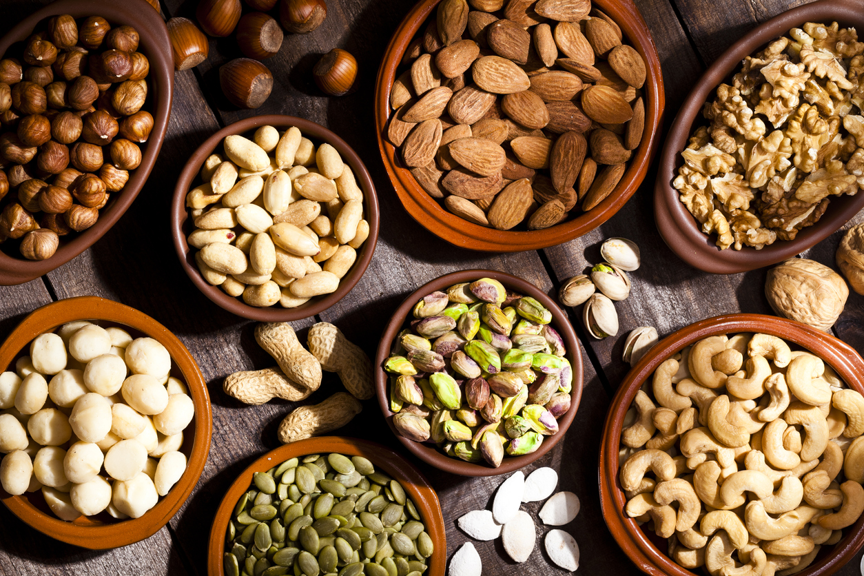 Top view of a rustic wood table filled with a large assortment of nuts like pistachios, hazelnut, pine nut, almonds, pumpkin seeds, peanuts, cashew and walnuts. Some nuts are in brown bowls and others are placed directly on the table. Predominant color is brown. DSRL studio photo taken with Canon EOS 5D Mk II and Canon EF 100mm f/2.8L Macro IS USM