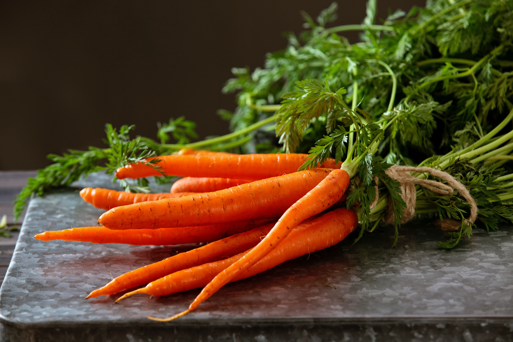 Heap of ripe carrots with leaves on dark rustic table.