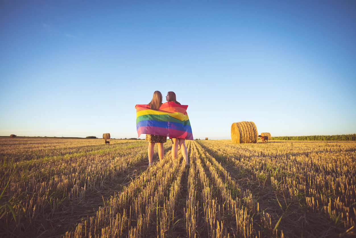 Lesbian couple with LGBT flag on a cropped field