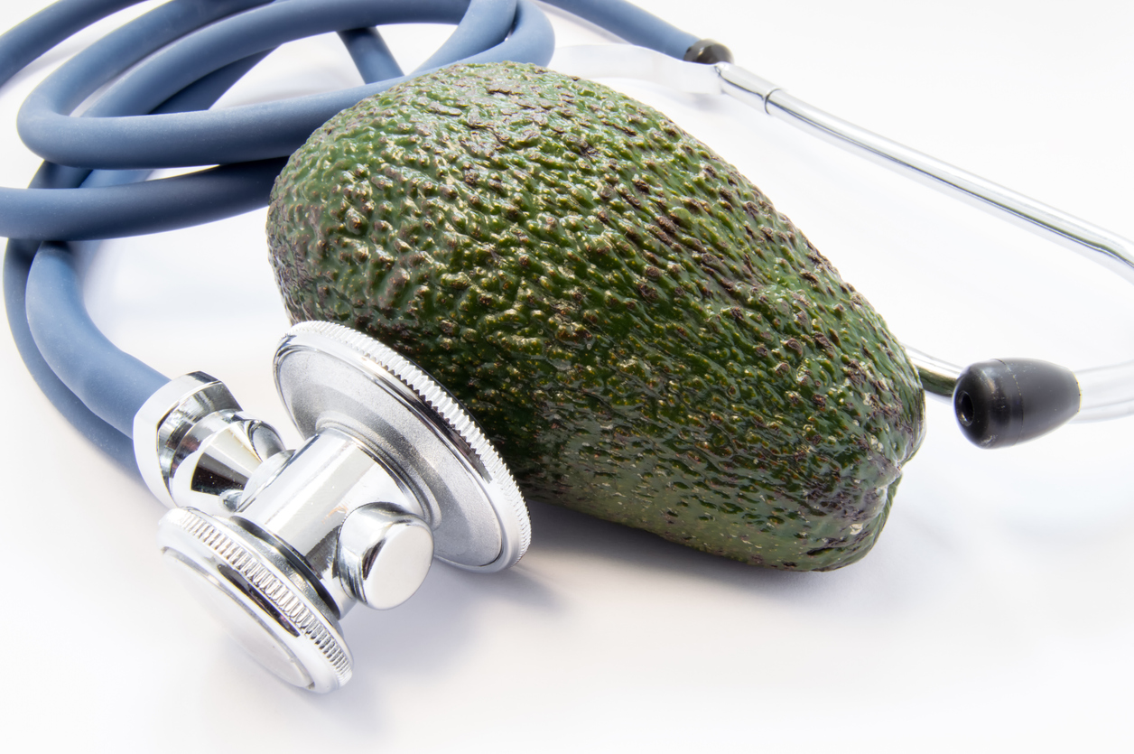 Green avocado raw fruit lies surrounded by stethoscope, which analyse it. Facts and benefits of avocados as tasty, nutritious and beneficial food ingredient healthy relating to dietetic food