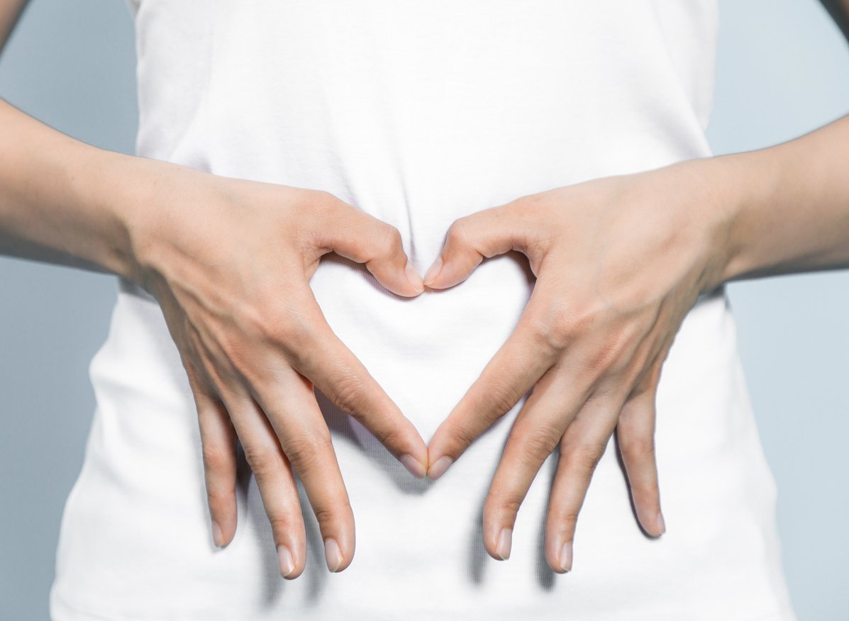 young woman who makes a heart shape by hands on her stomach.