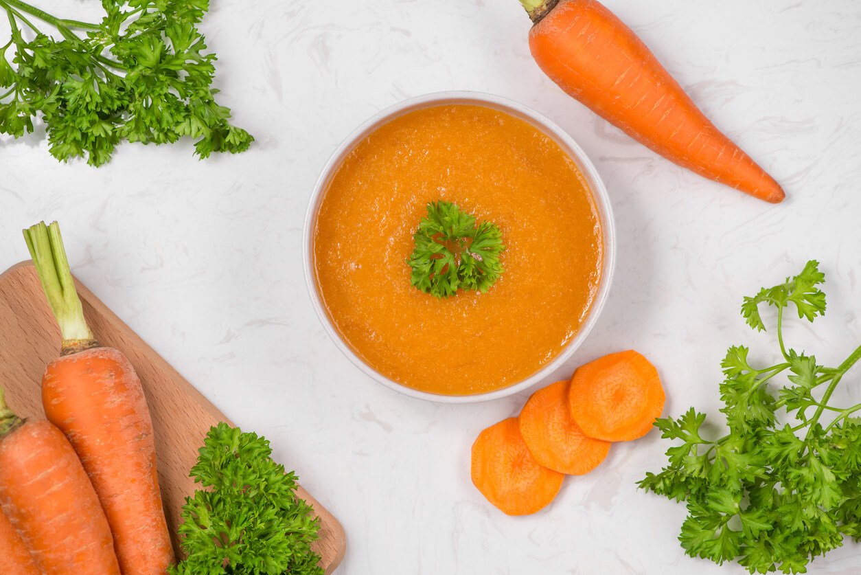 carrot soup with cream and parsley on white stone background top view copy space