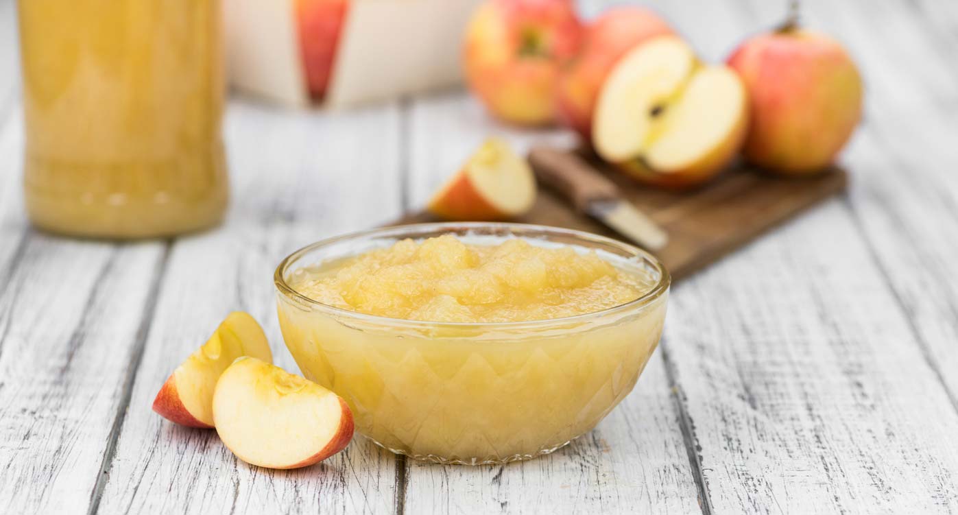 Homemade applesauce in bowl with apples nearby