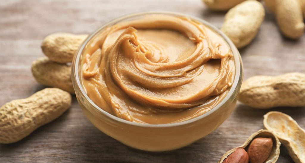 A bowl of peanut butter with peanuts around it