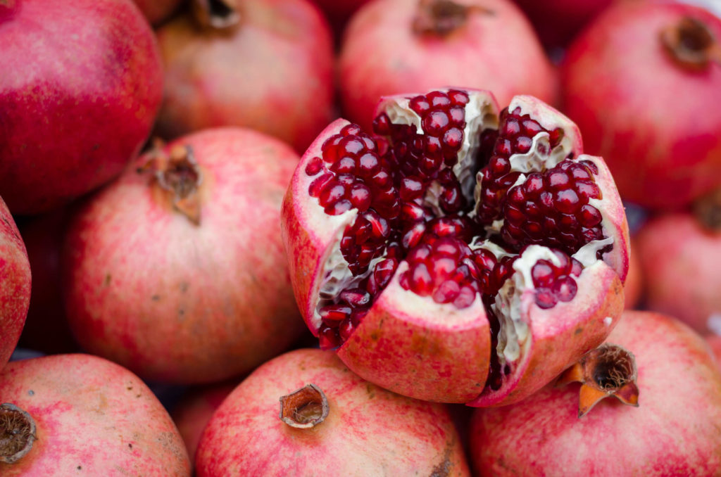 A pomegranate cut open with arils showing on top of a pile of pomegranates