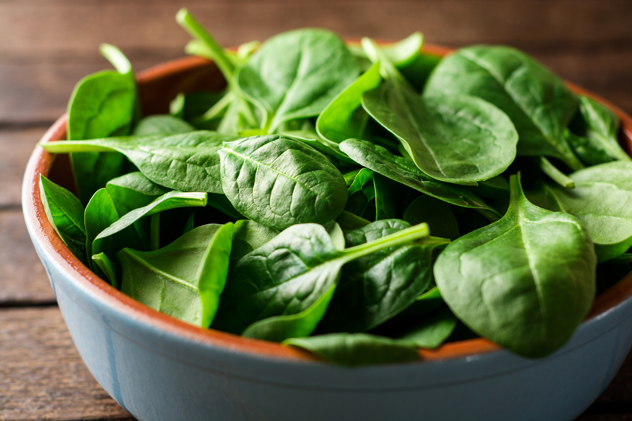 Fresh spinach leaves in bowl on rustic wooden table. Selective focus.