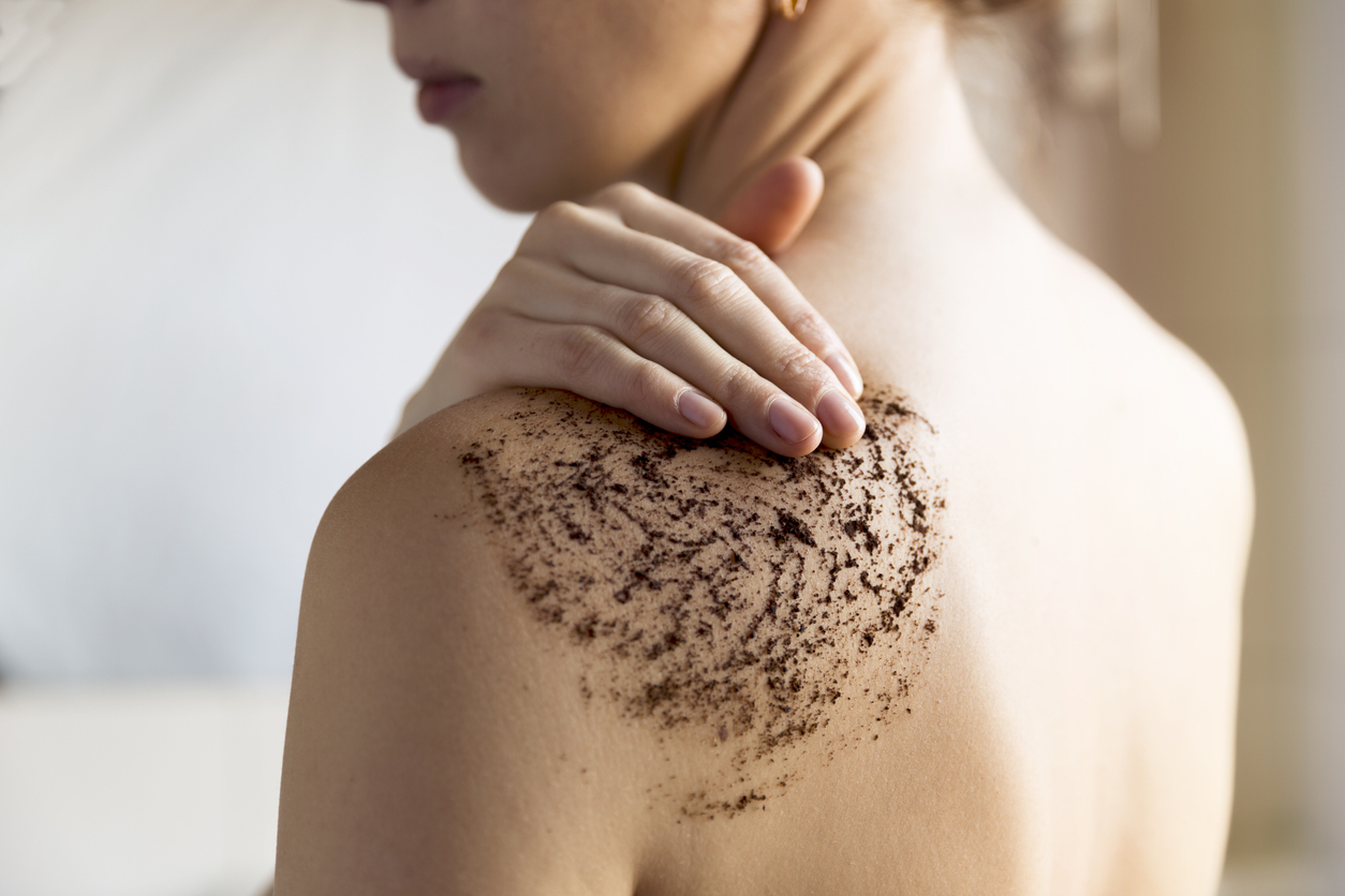 Beauty, spa and healthy skin concept - woman cleans skin of the body with coffee scrub in bathroom.